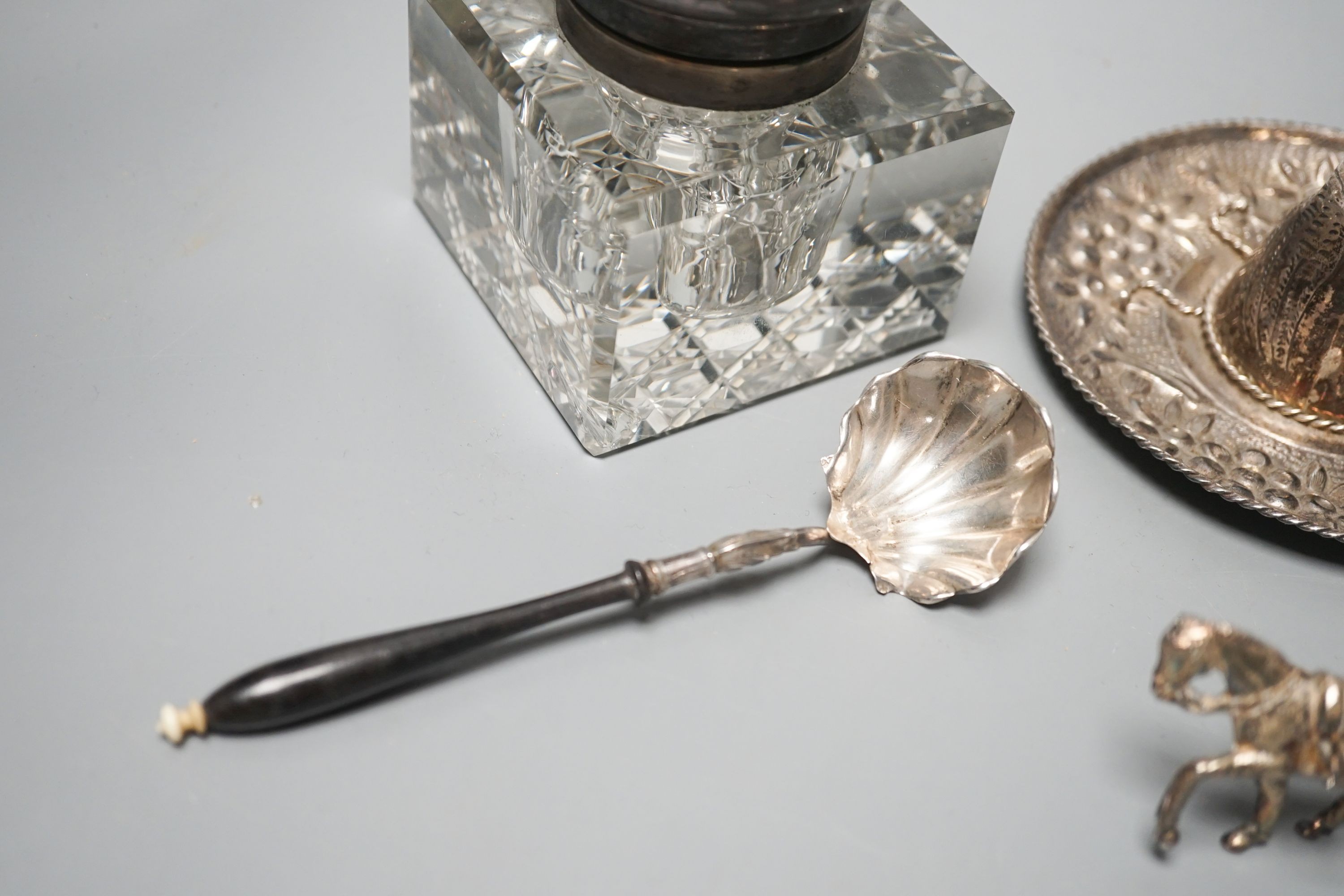 A silver mounted glass inkwell, A Mexican white metal miniature sombrero, a white metal caddy spoon and a filigree horse and carriage.